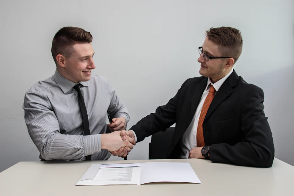 Two advisors shaking hands over a signed agreement